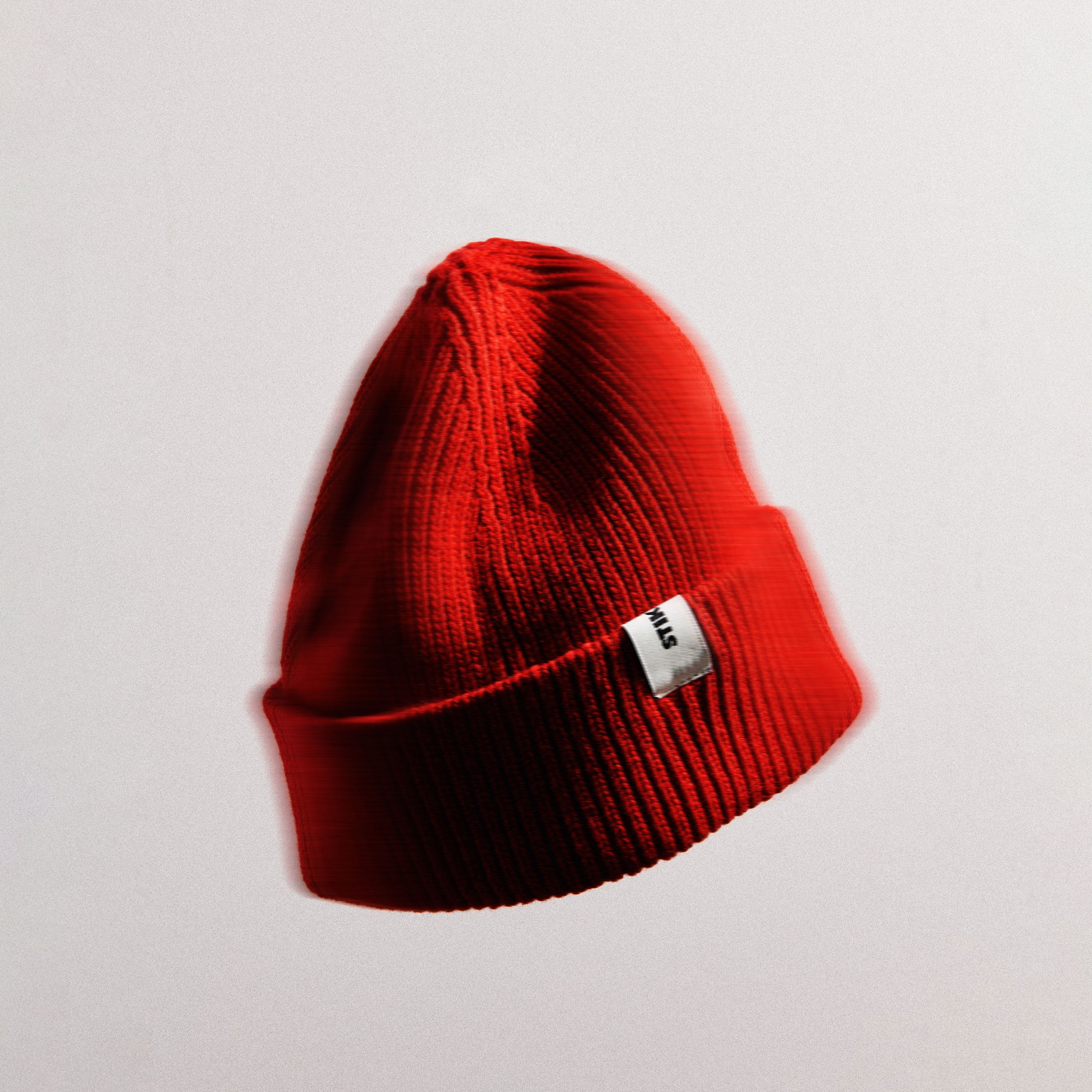 Red Stiksen beanie with a white label on a light grey background
