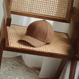 Brown linen baseball cap placed on woven wooden chair in warm indoor setting