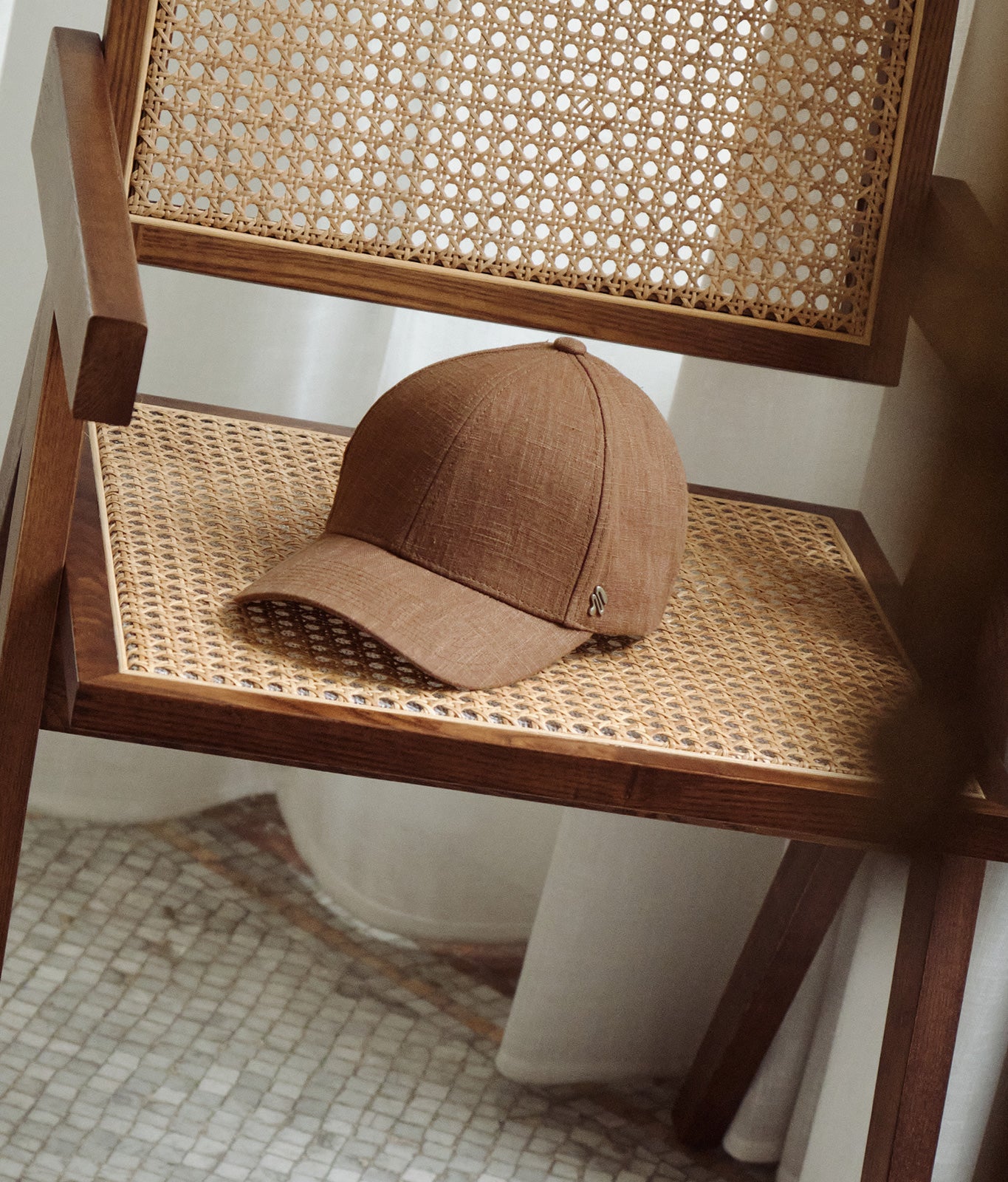 Brown linen baseball cap placed on woven wooden chair in warm indoor setting
