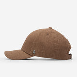 Brown linen baseball cap side view with curved brim and metal logo detail