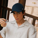 Stiksen 107 Linen Indigo baseball cap worn by model indoors in warm ambient lighting